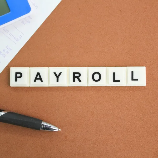Scrabble tiles spelling "Payroll" next to a calculator and receipt